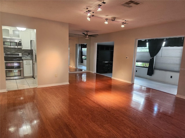 unfurnished living room with ceiling fan, a textured ceiling, and light wood-type flooring