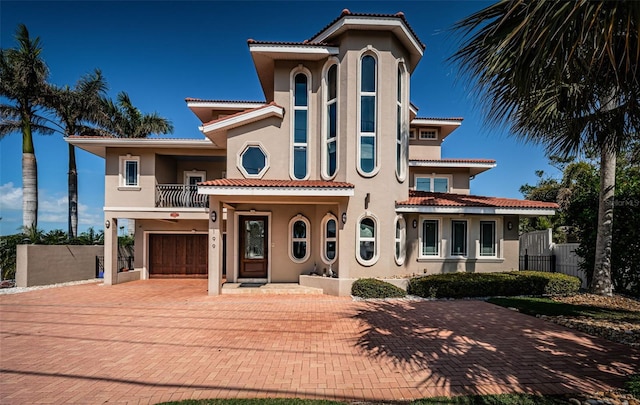 mediterranean / spanish home featuring a balcony, a tile roof, decorative driveway, and stucco siding