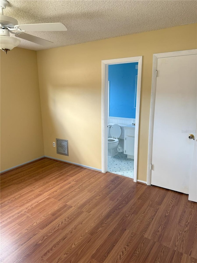 unfurnished bedroom featuring ceiling fan, wood-type flooring, a textured ceiling, and ensuite bathroom