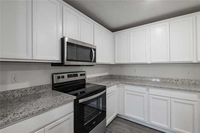 kitchen featuring wood-type flooring, appliances with stainless steel finishes, white cabinets, and light stone counters