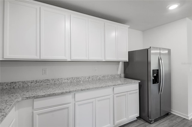 kitchen with stainless steel refrigerator with ice dispenser, light stone countertops, white cabinets, and light hardwood / wood-style flooring