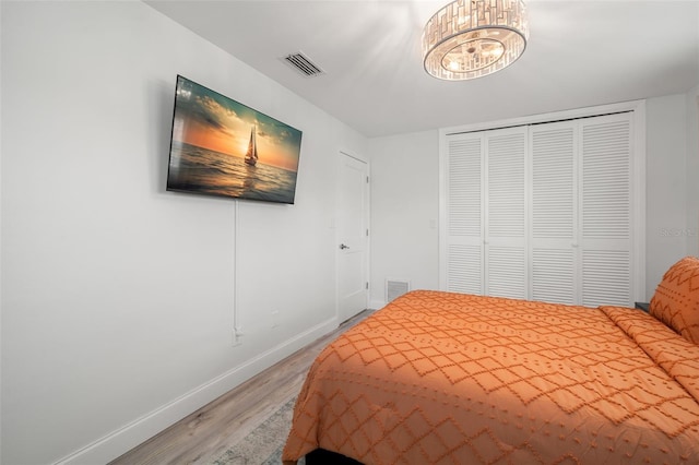 bedroom featuring an inviting chandelier, wood-type flooring, and a closet