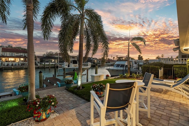 patio terrace at dusk featuring a water view and a dock