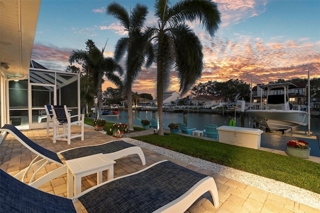 patio terrace at dusk featuring a yard, a dock, glass enclosure, and a water view