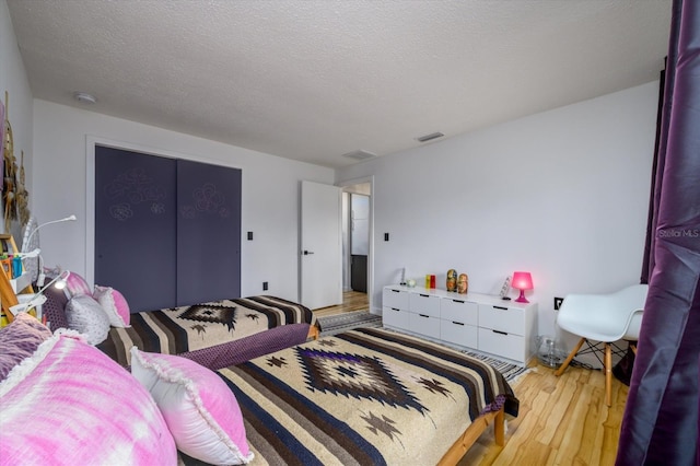 bedroom featuring a textured ceiling, a closet, light wood-type flooring, and visible vents