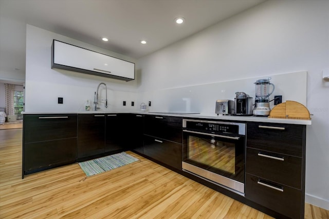 bar featuring recessed lighting, light wood-style flooring, a sink, and oven