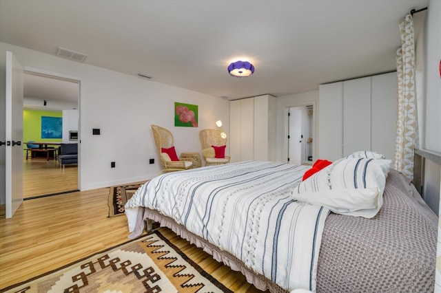 bedroom featuring two closets, baseboards, visible vents, and wood finished floors