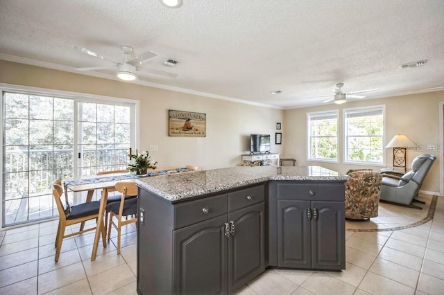 kitchen featuring ceiling fan, ornamental molding, a center island, and light tile patterned floors