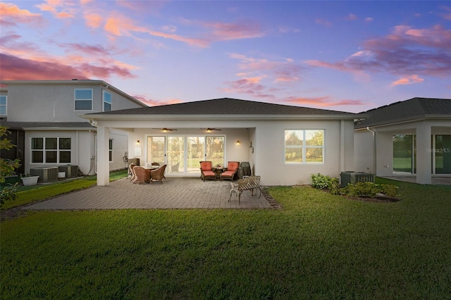 back house at dusk with ceiling fan, a patio area, cooling unit, and a lawn