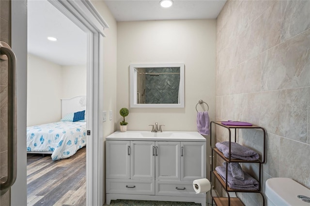 ensuite bathroom with connected bathroom, tile walls, vanity, and wood finished floors