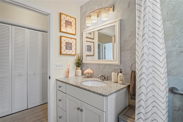 bathroom with tasteful backsplash, a closet, wood finished floors, vanity, and tile walls