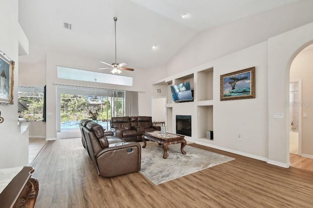 living room with ceiling fan, hardwood / wood-style flooring, high vaulted ceiling, and built in shelves