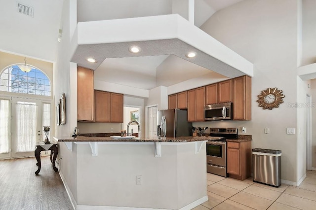 kitchen with sink, dark stone countertops, a kitchen breakfast bar, stainless steel appliances, and a high ceiling