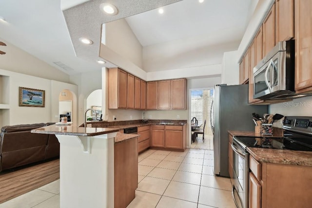 kitchen with dark stone countertops, a kitchen breakfast bar, light tile patterned floors, kitchen peninsula, and stainless steel appliances