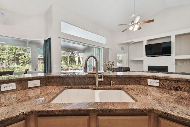 kitchen with dark stone countertops, sink, a wealth of natural light, and ceiling fan