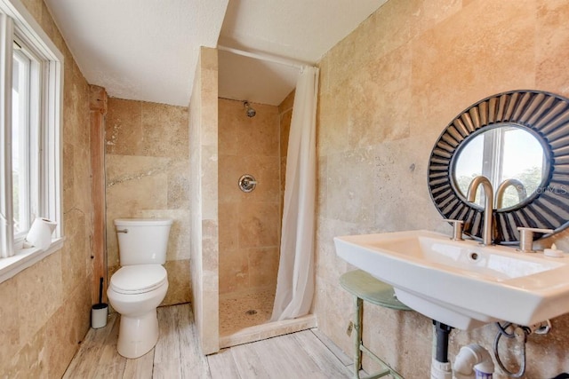 bathroom with toilet, a shower stall, a sink, and tile walls