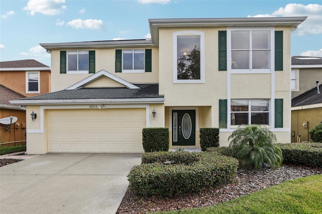 multi unit property with a garage, driveway, roof with shingles, and stucco siding