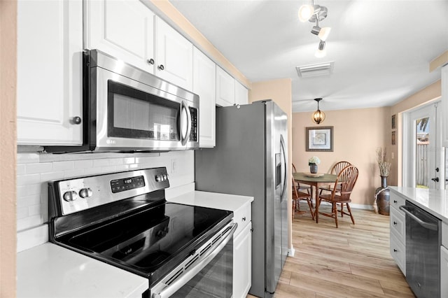 kitchen with hanging light fixtures, stainless steel appliances, white cabinets, decorative backsplash, and light wood-type flooring