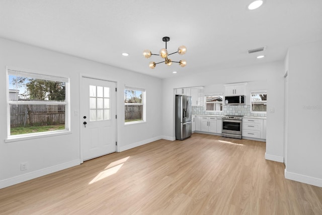 kitchen featuring appliances with stainless steel finishes, white cabinets, backsplash, hanging light fixtures, and light wood-type flooring