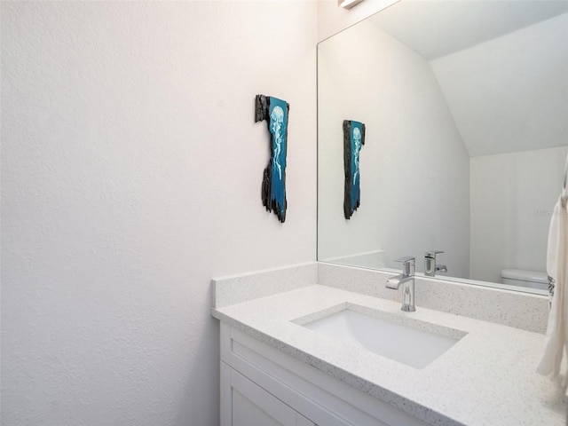 bathroom featuring lofted ceiling, vanity, and toilet