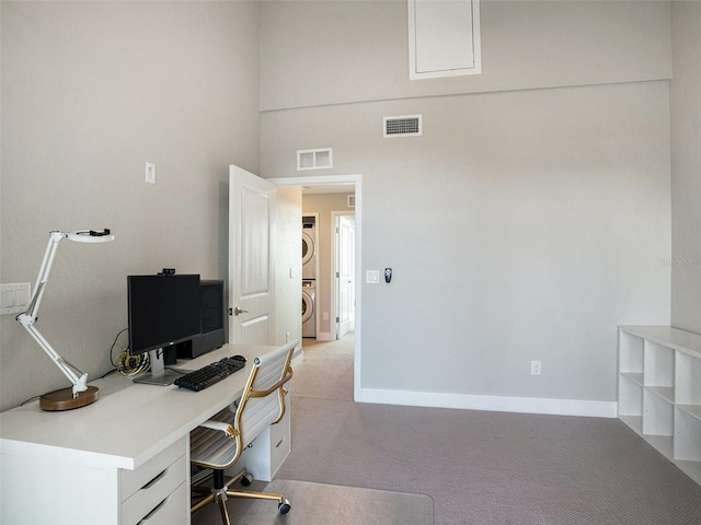 home office with light colored carpet, a high ceiling, and stacked washing maching and dryer