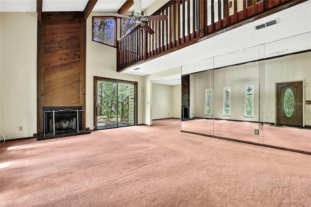 unfurnished living room featuring beamed ceiling, a large fireplace, carpet, ceiling fan, and a high ceiling