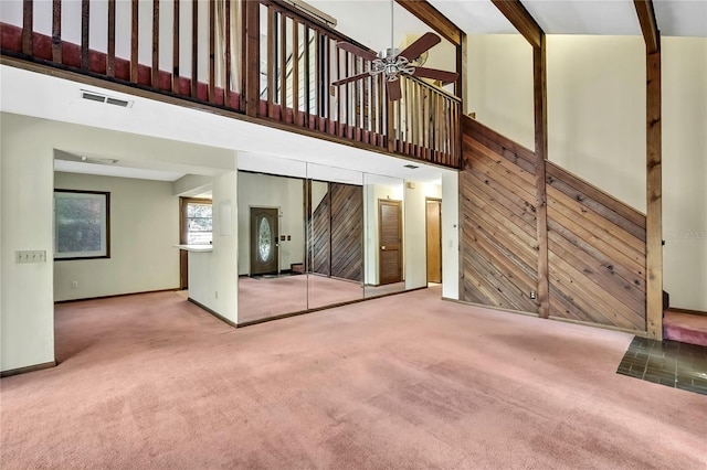 unfurnished living room with ceiling fan, carpet flooring, a high ceiling, and wooden walls