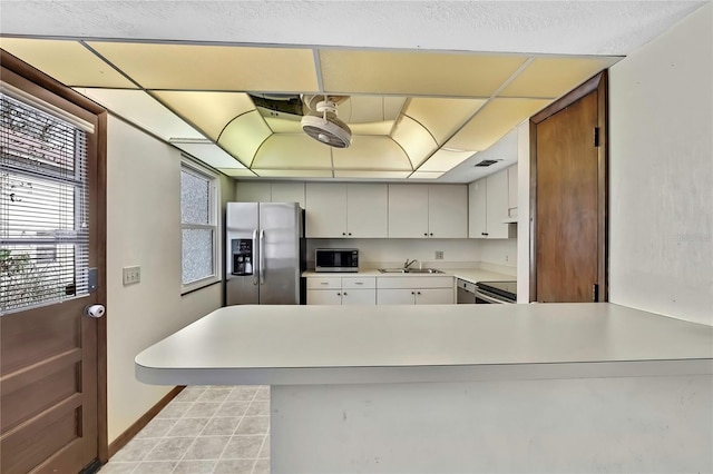 kitchen featuring appliances with stainless steel finishes, sink, light tile patterned floors, white cabinetry, and kitchen peninsula