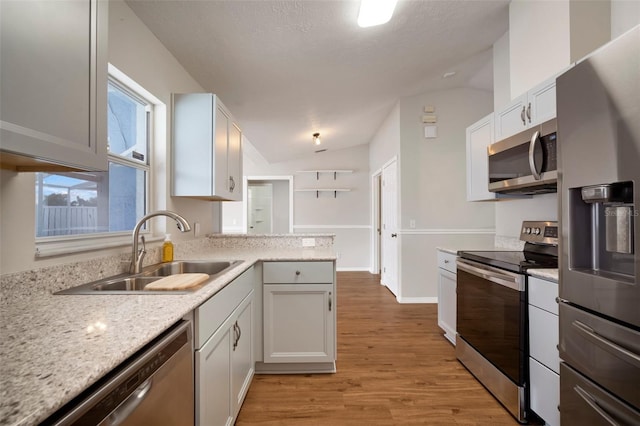 kitchen with lofted ceiling, sink, white cabinets, light hardwood / wood-style floors, and stainless steel appliances