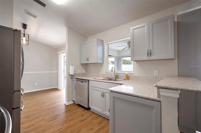 kitchen with sink, light stone counters, a textured ceiling, appliances with stainless steel finishes, and light hardwood / wood-style floors