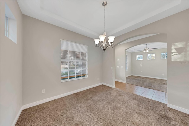 carpeted empty room with a tray ceiling, tile patterned flooring, arched walkways, and baseboards