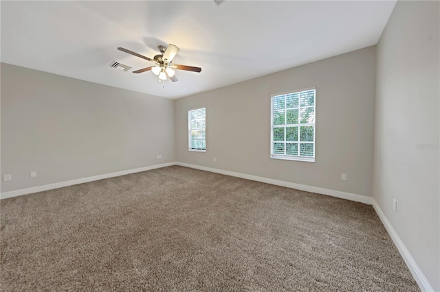 empty room with carpet floors, a ceiling fan, visible vents, and baseboards