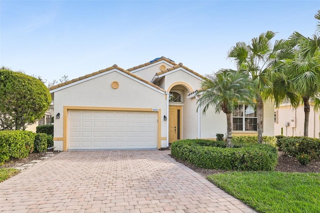 mediterranean / spanish-style home featuring a garage, decorative driveway, a tile roof, and stucco siding