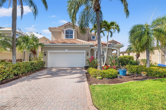 mediterranean / spanish-style home with a tiled roof, decorative driveway, an attached garage, and stucco siding