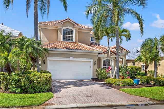 mediterranean / spanish home with a garage, decorative driveway, a tile roof, and stucco siding