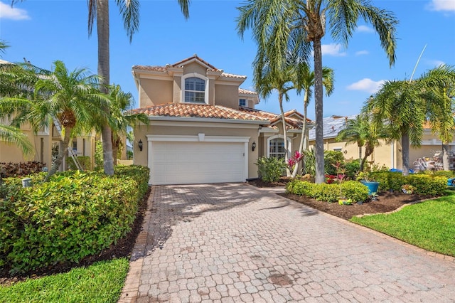 mediterranean / spanish house with a garage, decorative driveway, a tiled roof, and stucco siding