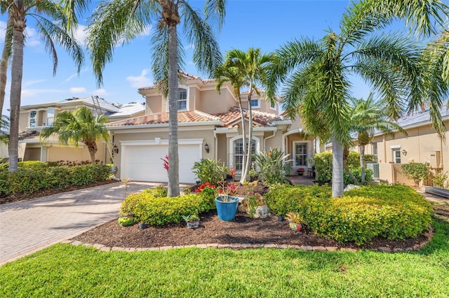 mediterranean / spanish-style home with a garage, a tiled roof, decorative driveway, and stucco siding