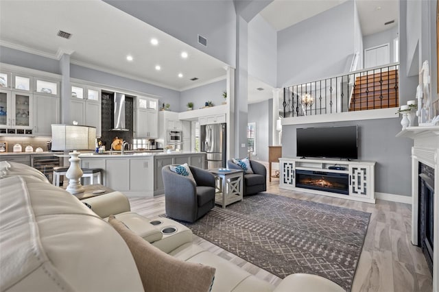 living room featuring a lit fireplace, light wood-type flooring, a towering ceiling, and visible vents