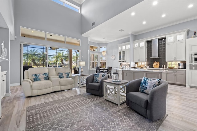 living area with recessed lighting, a towering ceiling, baseboards, ornamental molding, and light wood-type flooring