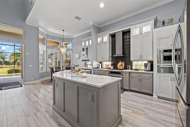 kitchen with gray cabinetry, visible vents, wall chimney range hood, appliances with stainless steel finishes, and an island with sink