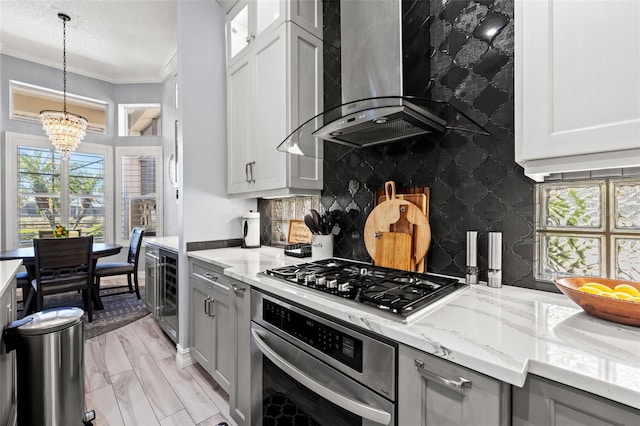 kitchen with light stone counters, stainless steel appliances, backsplash, wall chimney exhaust hood, and crown molding