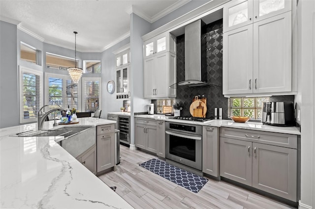 kitchen featuring gray cabinetry, stainless steel appliances, a sink, ornamental molding, and wall chimney range hood