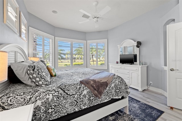 bedroom featuring arched walkways, baseboards, a ceiling fan, and light wood-style floors