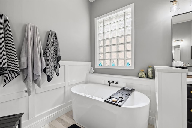 bathroom with a decorative wall, wainscoting, vanity, wood finished floors, and a freestanding tub