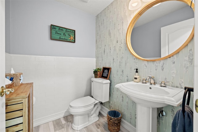 half bath featuring wood finished floors, baseboards, toilet, and wallpapered walls