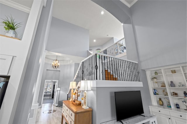 living room with light wood finished floors, stairway, ornamental molding, an inviting chandelier, and a high ceiling