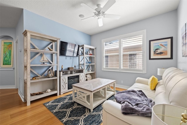 interior space with arched walkways, wood finished floors, a ceiling fan, and baseboards