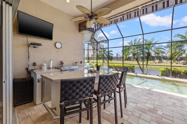 view of patio / terrace featuring an outdoor kitchen, a lanai, outdoor wet bar, a water view, and a ceiling fan