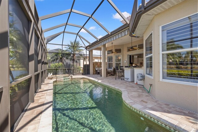 view of pool featuring glass enclosure, a pool with connected hot tub, a patio area, and a ceiling fan