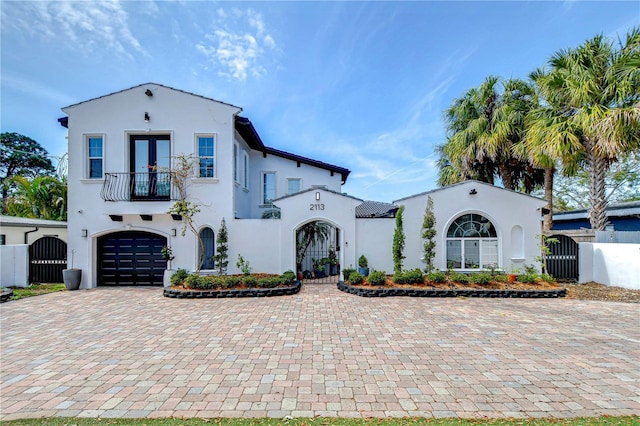 mediterranean / spanish-style house featuring an attached garage, a balcony, french doors, decorative driveway, and stucco siding